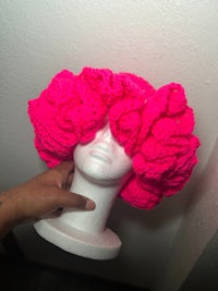 a person holding a pink crocheted hat in front of a mannequin