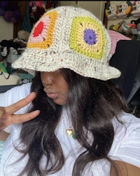 a woman wearing a crocheted hat and making a peace sign