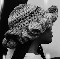 a black and white photo of a woman wearing a crocheted hat