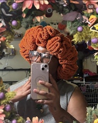 a woman taking a selfie in a crocheted afro hat