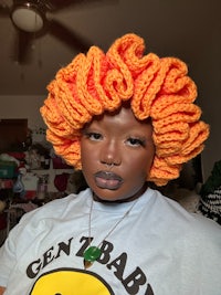 a black woman wearing an orange crocheted afro wig